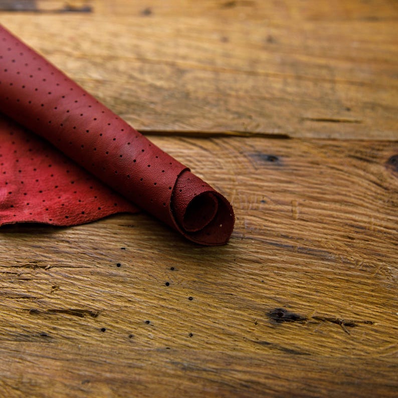 May include: A roll of red leather with a dotted pattern. The leather is rolled up and lying on a wooden surface.