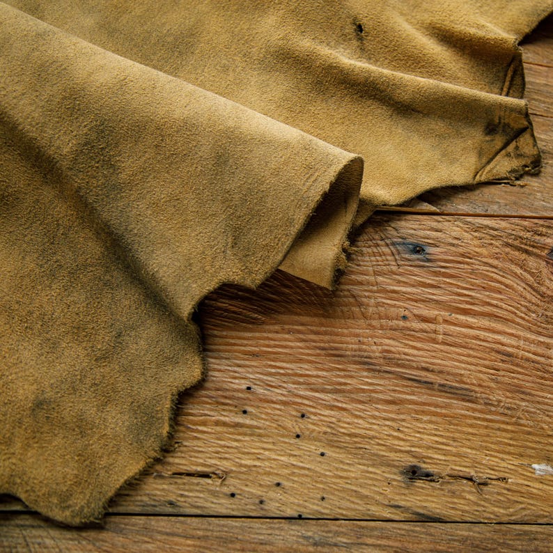 Puede incluir: Un trozo de cuero marr&oacute;n con una textura rugosa est&aacute; doblado sobre una superficie de madera. El cuero tiene un aspecto desgastado y envejecido.