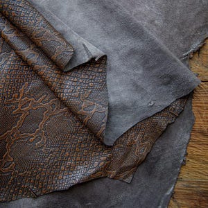 May include: Two pieces of leather, one with a brown snakeskin pattern and the other a solid gray. The leather is folded and overlapping.