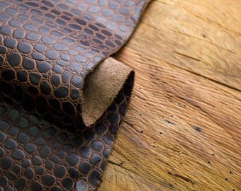 May include: Close-up of a brown leather with a crocodile pattern, rolled up and placed on a wooden surface.