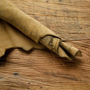 Puede incluir: Un trozo de cuero marr&oacute;n enrollado y colocado sobre una superficie de madera.