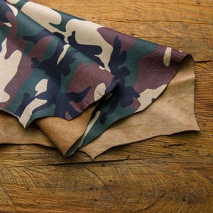 May include: A piece of camouflage leather folded over a piece of brown leather. The leather is on a wooden surface.