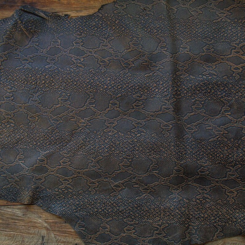 May include: A piece of brown faux snakeskin leather with a textured pattern. The leather has a dark brown background with a lighter brown snakeskin pattern.