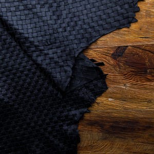 May include: A piece of black woven leather with a textured surface. The leather is laid out on a wooden surface.