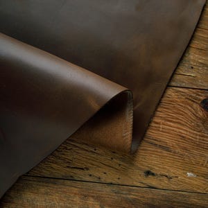 May include: A piece of brown leather folded over on a wooden surface. The leather has a natural, distressed look.