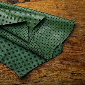 May include: A folded piece of green leather with a dotted pattern. The leather is folded in a triangular shape and is lying on a wooden surface.
