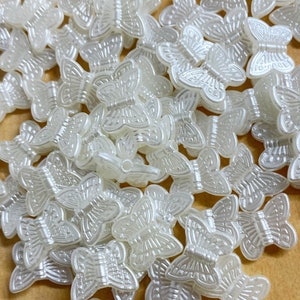 May include: A large pile of off-white plastic butterfly beads. Butterfly beads. NOT pure white.