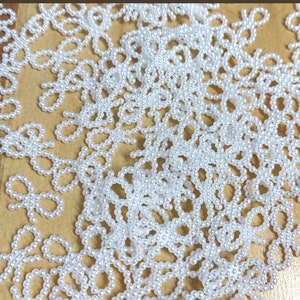 May include: A close-up of a large quantity of white pearl beads arranged in a pattern of bows. The beads are scattered on a brown surface.