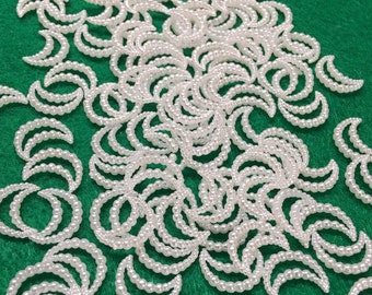 May include: A large quantity of white pearl crescent moon shapes on a green felt background.