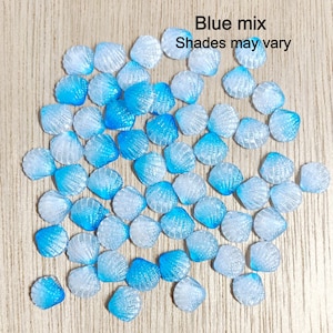 May include: A collection of blue and white seashell-shaped resin embellishments. The shells are various shades of blue and white, with a shimmery finish. Blue mix. Shades may vary.