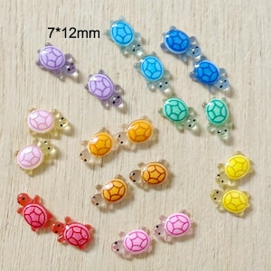 May include: A collection of colorful, miniature turtle-shaped embellishments. The turtles are in various colors, including blue, green, yellow, orange, pink, and purple. Each turtle measures 7mm x 12mm.
