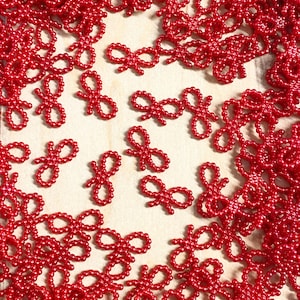 May include: A large quantity of small, red, pearl-like beads arranged in the shape of bows. The beads are scattered on a light brown surface.