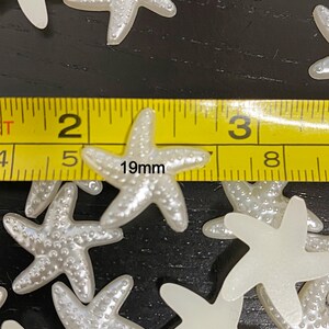 May include: White pearl-like starfish embellishments with a textured surface. The starfish are approximately 19mm in size.