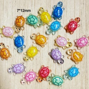 May include: A collection of small, translucent turtle-shaped charms in various colors including pink, yellow, blue, green, orange, and purple. Each turtle features a detailed shell pattern and measures 7*12mm as indicated by the text.