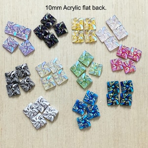 May include: A collection of 10mm acrylic flat back embellishments in various colors. The embellishments are square-shaped with a swirling floral design. Colors include purple, black, gold, pink, green, blue, and silver.