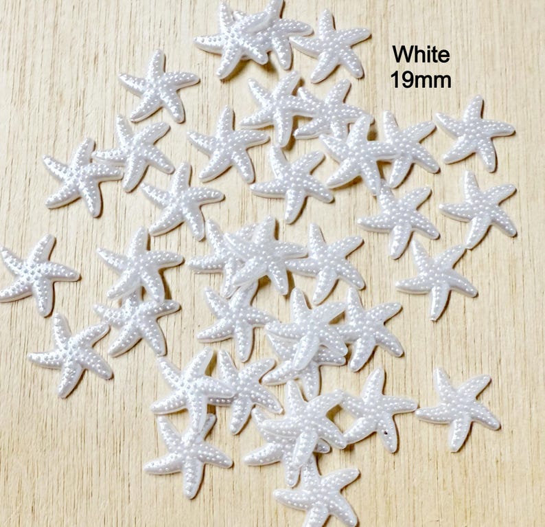 May include: A collection of white starfish embellishments, each measuring 19mm, scattered on a light wood surface. The starfish have a textured surface with small, raised dots. The word "White" is displayed in the image.