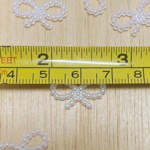 May include: White pearl bow embellishments on a wooden surface with a measuring tape showing 5 inches.