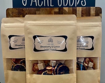 May include: Three brown paper bags with clear plastic windows, each containing a cocktail infusion kit. The bags are labeled "Strawberry & Lemon Cocktail Infusion Kit" and "Berry & Lemon Cocktail Infusion Kit". The kits contain dried fruit, sugar cubes, and other ingredients.
