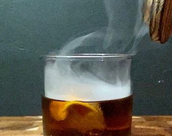 May include: A glass of amber-colored liquid with a lemon twist, smoke rising from the glass.