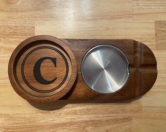 May include: A wooden coaster set with a round coaster featuring the letter "C" and a rectangular coaster with a circular indentation for a glass or mug. The coaster set is made of dark wood.