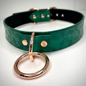 K&ouml;nnte beinhalten: Ein gr&uuml;nes Lederhalsband mit einem Rosenholz-Blatt-Muster und einem Rosenholz-Ring.