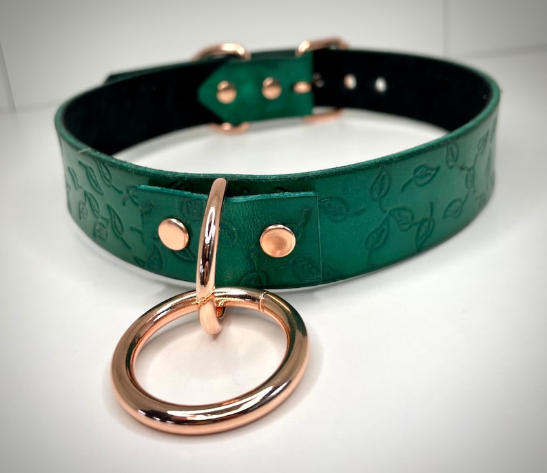 K&ouml;nnte beinhalten: Ein gr&uuml;nes Lederhalsband mit einem Rosenholz-Blatt-Muster und einem Rosenholz-Ring.