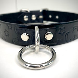 May include: Black leather choker with a silver metal ring and a moon and star embossed pattern.