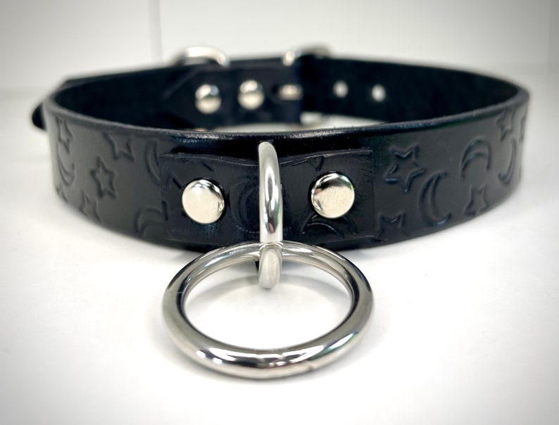 May include: Black leather choker with a silver metal ring and a moon and star embossed pattern.