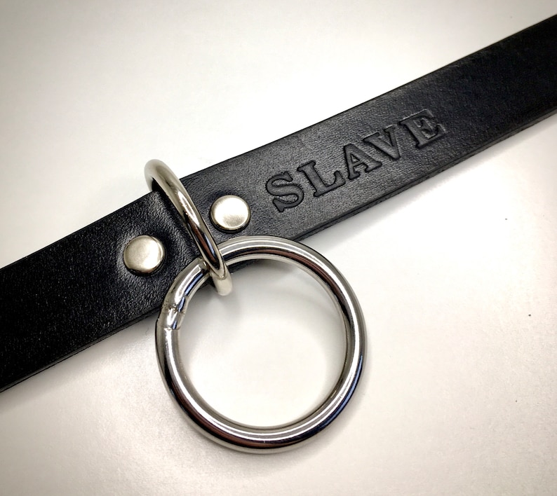 May include: Black leather collar with a silver ring and the word "SLAVE" embossed on the leather.