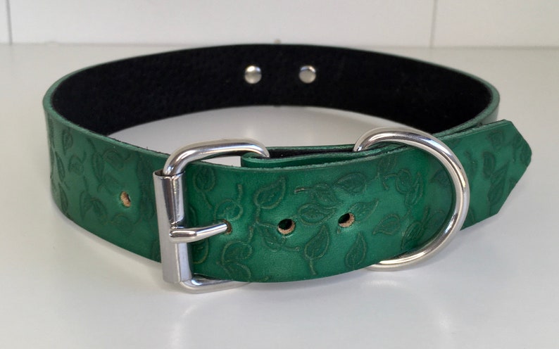K&ouml;nnte beinhalten: Ein gr&uuml;nes Lederhundekragen mit einer silbernen Schnalle und einem D-Ring. Das Halsband hat ein gepr&auml;gtes Blattmotiv.