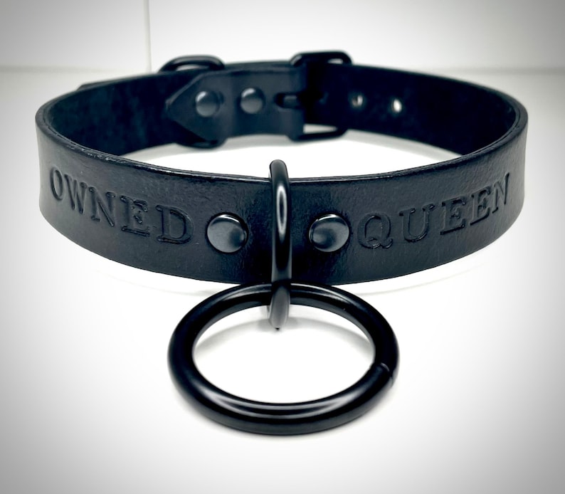 May include: Black leather choker with a metal ring and the words "OWNED QUEEN" embossed on the front.