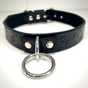 May include: Black leather choker with a silver metal ring and a star and crescent moon pattern.