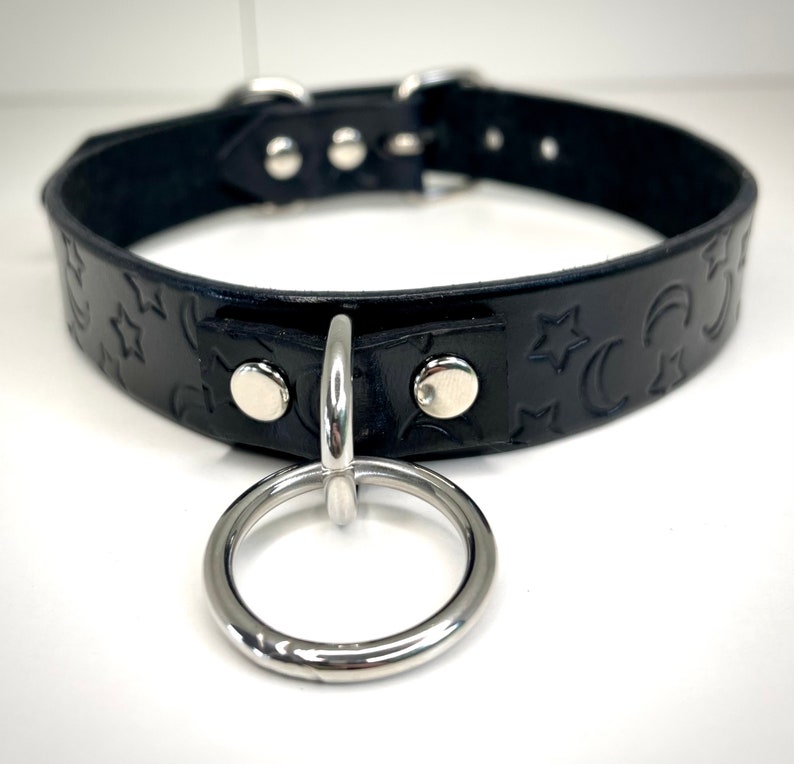 May include: Black leather choker with a silver metal ring and a star and crescent moon pattern.