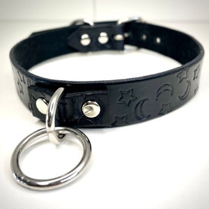 May include: Black leather choker with a silver ring and moon and star embossed design.