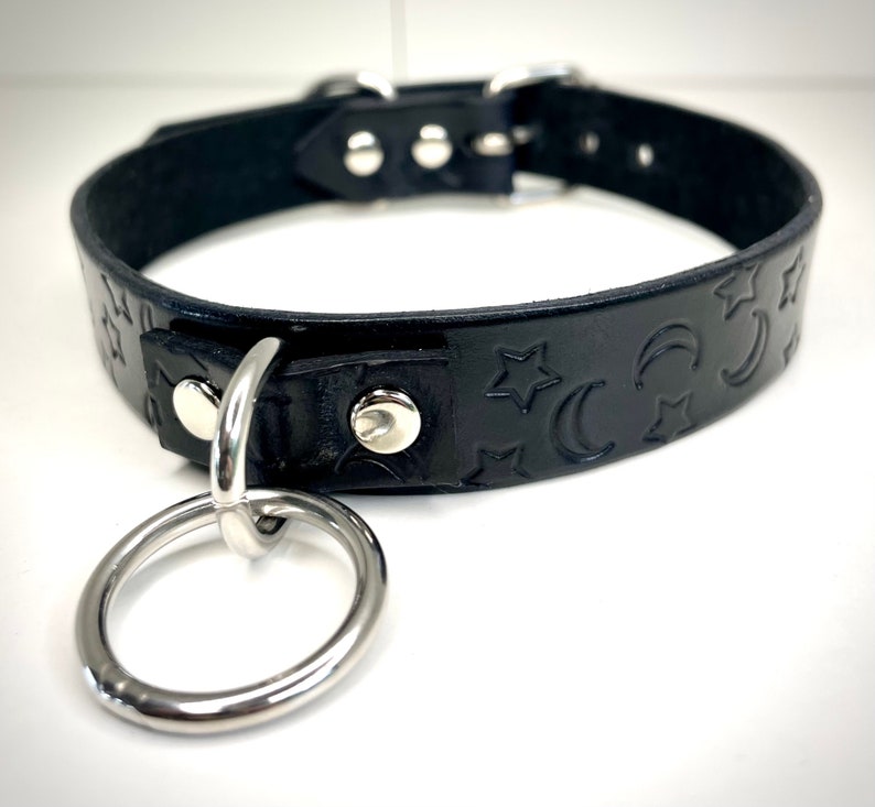 May include: Black leather choker with a silver ring and moon and star embossed design.