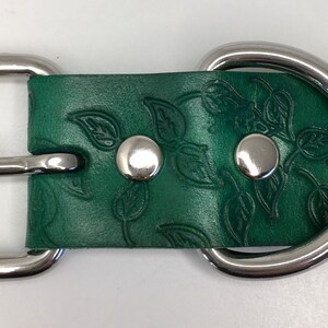 K&ouml;nnte beinhalten: Ein gr&uuml;nes Lederhundekragen mit einer silbernen Schnalle und einem D-Ring. Das Leder ist mit einem Blattmotiv gepr&auml;gt.