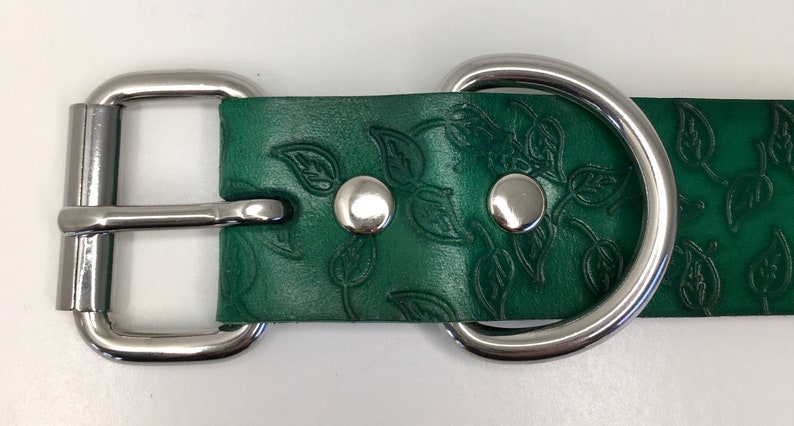 K&ouml;nnte beinhalten: Ein gr&uuml;nes Lederhundekragen mit einer silbernen Schnalle und einem D-Ring. Das Leder ist mit einem Blattmotiv gepr&auml;gt.