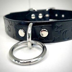 May include: Black leather choker with a silver ring and a star and crescent moon pattern.