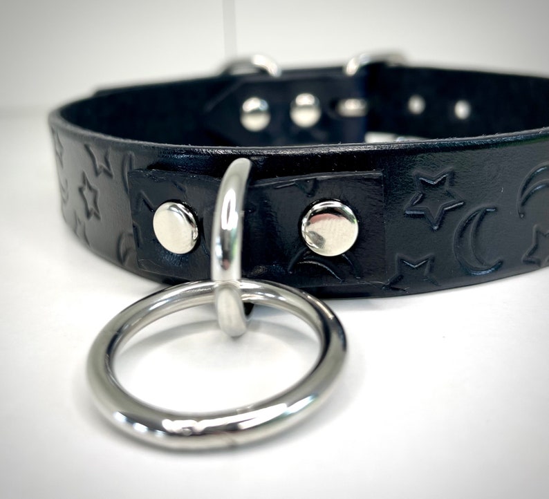 May include: Black leather choker with a silver ring and a star and crescent moon pattern.