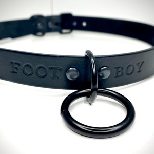 May include: Black leather collar with a metal ring and the words "FOOT BOY" embossed on the front.