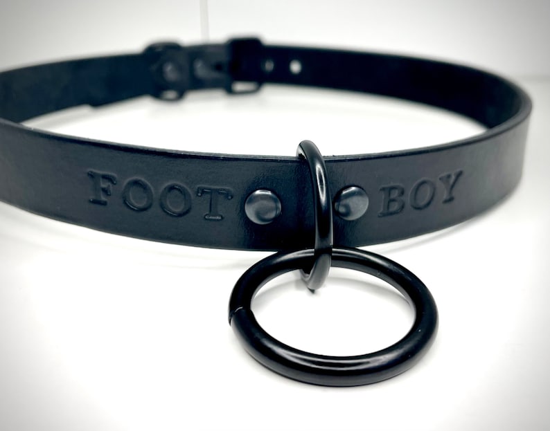 May include: Black leather collar with a metal ring and the words "FOOT BOY" embossed on the front.