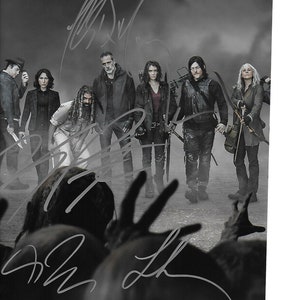 Könnte beinhalten: Schwarzweißfoto einer Gruppe von Personen, die vor einem dunklen Hintergrund stehen. Die Personen tragen alle dunkle Kleidung und haben einen ernsten Gesichtsausdruck. Das Foto ist von den Schauspielern der Fernsehserie The Walking Dead signiert.