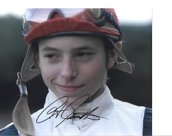 Könnte beinhalten: Porträt einer Person mit einer rot-beigen Jockey-Kappe mit Brille und einem weißen Hemd mit Kragen. Die Person lächelt, und am unteren Bildrand befindet sich eine Unterschrift in schwarzer Tinte.