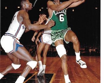 Könnte beinhalten: Vintage-Foto eines Basketballspiels. Ein Spieler in einem grünen Celtics-Trikot mit der Nummer 6 ist in der Luft und hält einen Basketball. Ein anderer Spieler trägt eine weiß-blaue Uniform. Das Bild ist signiert. Der Platz ist aus Holz.