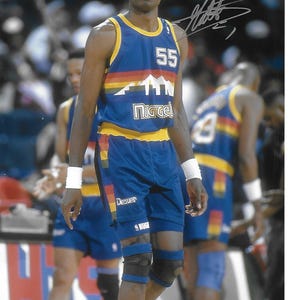 Può includere: Un giocatore di basket che indossa una maglia blu e gialla con il numero 55 sul davanti. La maglia ha la scritta "Nuggets" sul davanti e la scritta "Denver" sui pantaloncini. Il giocatore indossa ginocchiere e guarda dritto.