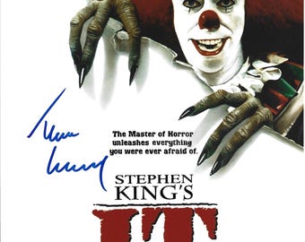 May include: A poster for Stephen King's IT featuring a clown with a white face, red nose, and red hair, reaching out with clawed hands. The text reads: The Master of Horror unleashes everything you were ever afraid of. STEPHEN KING'S IT. Includes a blue ink signature.