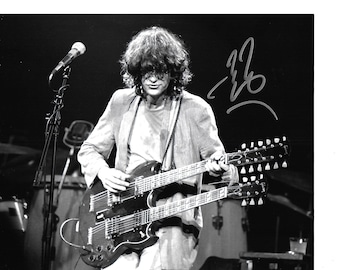 Könnte beinhalten: Schwarzweißfoto eines Musikers, der eine Doppelhals-E-Gitarre spielt. Der Musiker trägt eine Jacke und hat langes Haar. Die Unterschrift "JB" ist in der oberen rechten Ecke des Bildes zu sehen.