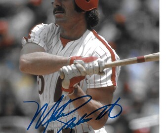 May include: A baseball player in a red helmet and a white and red striped uniform, holding a wooden bat. The player is wearing batting gloves and has a mustache. The image is signed in blue ink.