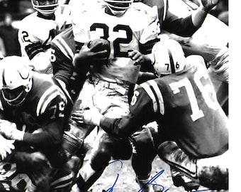 Könnte beinhalten: Schwarz-Weiß-Fotografie eines American-Football-Spiels. Ein Spieler mit der Nummer 32 auf seinem Trikot läuft mit dem Ball, umgeben von anderen Spielern in Helmen und Uniformen. Das Bild ist mit blauer Tinte signiert.