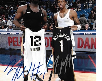 May include: Two basketball jerseys, one white with the number 12 and the name "Morant" on it, and one black with the number 1 and the name "Williamson" on it. The jerseys are being held by two basketball players, one wearing a black tank top and the other wearing a white tank top. The jerseys are signed with the names "Ja" and "Zion".
